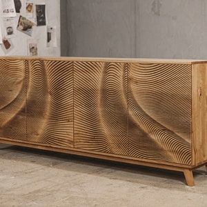 Puede incluir: Un aparador de madera con un patrón único en forma de ola tallado en las puertas. El mueble está hecho de madera de color claro y tiene cuatro puertas. La marca "Oaky Oak Furniture" es visible en la esquina superior derecha.