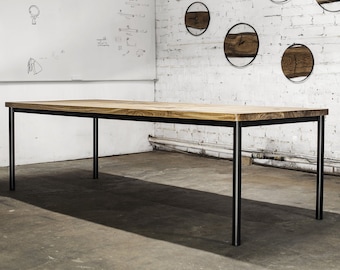 May include: A rectangular wooden table with a light brown surface and black metal legs. The table is in a room with a white brick wall and round wooden wall decor.
