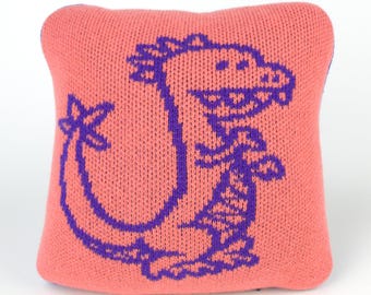 25cm knitted dinosaur cushion. Coral pink & purple merino lambswool. Handmade in UK.