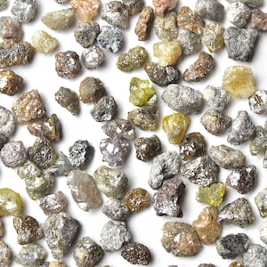 May include: A collection of small, rough, gray and yellow diamonds. The diamonds are scattered on a white surface.