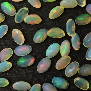 May include: A collection of oval-shaped opals with a variety of iridescent colors, including green, blue, and pink. The opals are arranged on a dark background.