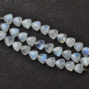 May include: Strands of faceted, triangular moonstone beads. The beads are a translucent white with flashes of blue and iridescent color. The beads are strung on thin, silver-colored wire, and are displayed against a dark background.