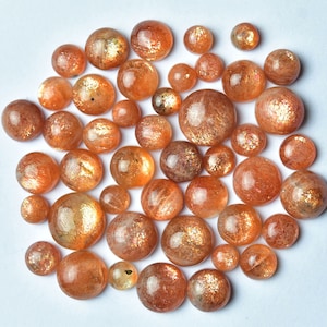 May include: A collection of round, polished sunstone cabochons in various sizes. The stones are a mix of orange, brown, and gold colors with a shimmering, iridescent effect.