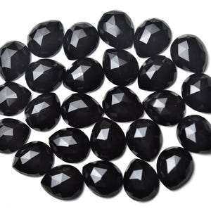 May include: A collection of faceted, black gemstones with a teardrop shape. The gemstones are arranged closely together against a white background, showcasing their polished surfaces and reflective facets. These stones are suitable for jewelry making.