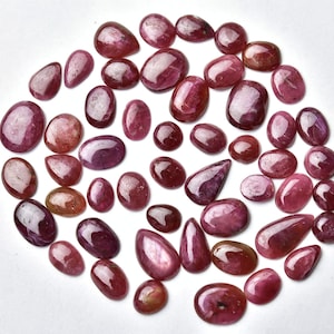 May include: A collection of 40+ pink and red gemstone cabochons. The cabochons are various shapes and sizes, with a smooth, polished finish.