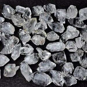 May include: A collection of clear quartz crystals, also known as Herkimer diamonds, with a variety of shapes and sizes. The crystals are faceted and have a natural, raw appearance.