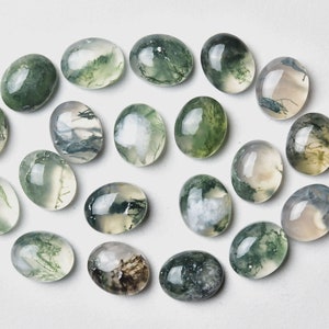 May include: A collection of twenty-one oval-shaped moss agate gemstones. The stones display a translucent appearance with green, white, and gray inclusions, set against a white background. These polished stones are suitable for jewelry making.