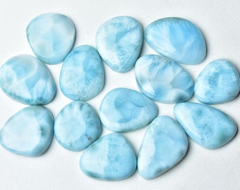 May include: A collection of 11 smooth, light blue, polished, natural gemstone cabochons. The stones have a cloudy, marbled pattern.