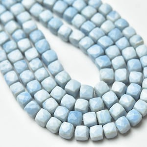 May include: A strand of light blue gemstone beads, each bead is faceted and has a square shape.
