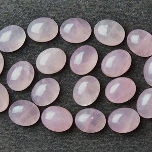 May include: A collection of 18 oval-shaped, pale pink rose quartz cabochons. The stones are smooth and polished, with a subtle shimmer.