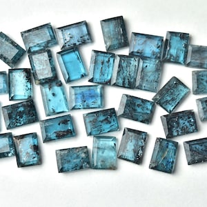 May include: A collection of 25 blue-green gemstone rectangular cabochons. The stones have a dark blue-green color with a slight shimmer. The stones are all approximately the same size and shape.