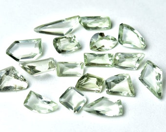 May include: A collection of pale green gemstone chips in various shapes and sizes. The chips are faceted and have a translucent appearance.