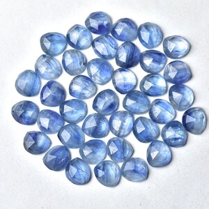 Puede incluir: Colecci&oacute;n de gemas facetadas de color azul claro con forma de coraz&oacute;n. Las gemas est&aacute;n dispersas sobre una superficie blanca, mostrando sus variados tonos de azul y cortes intrincados. Ideales para la creaci&oacute;n de joyas.