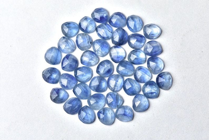 Puede incluir: Colecci&oacute;n de gemas facetadas de color azul claro con forma de coraz&oacute;n. Las gemas est&aacute;n dispersas sobre una superficie blanca, mostrando sus variados tonos de azul y cortes intrincados. Ideales para la creaci&oacute;n de joyas.