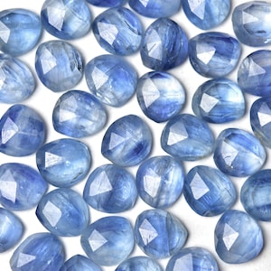 Puede incluir: Una colecci&oacute;n de gemas facetadas de color azul claro con una variedad de formas, incluyendo formas redondas y triangulares. Las gemas tienen una cualidad transl&uacute;cida, con vetas internas y una superficie pulida. La disposici&oacute;n es dispersa, mostrando la variedad de las piedras.