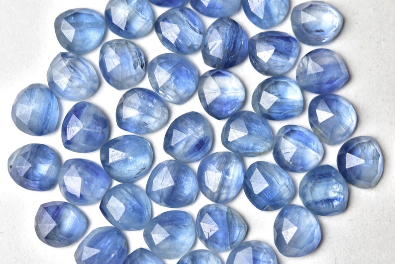 Puede incluir: Una colecci&oacute;n de gemas facetadas de color azul claro con una variedad de formas, incluyendo formas redondas y triangulares. Las gemas tienen una cualidad transl&uacute;cida, con vetas internas y una superficie pulida. La disposici&oacute;n es dispersa, mostrando la variedad de las piedras.