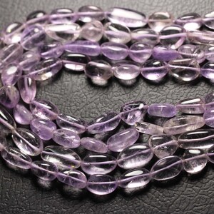 May include: A strand of pale lavender amethyst gemstone beads. The beads are oval shaped and have a smooth, polished finish.