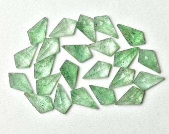 May include: A collection of twenty green and clear faceted gemstone points. The points are arranged in a random pattern on a white surface.