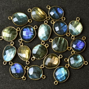 May include: A collection of 17 oval-shaped labradorite gemstone beads with gold-toned metal connector loops. The beads are a mix of blue, green, and gold colors.