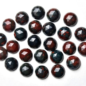 May include: A collection of faceted gemstone beads. The beads are a mix of dark red and dark teal colors, with a geometric cut that reflects light. The beads are round and appear to be made of a natural stone material.