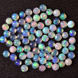 May include: A collection of iridescent opal cabochons, each with a unique play of color. The cabochons are round and have a smooth, polished finish. They are a beautiful shade of white with flashes of blue, green, and pink.