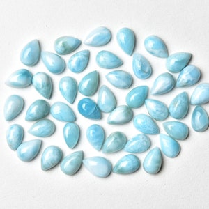 May include: A collection of light blue teardrop-shaped cabochon gemstones. The stones have a cloudy, marbled appearance.