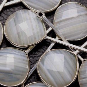 May include: A close-up of several silver-toned metal pendants with white agate stones. The stones have a striated pattern and are oval-shaped.