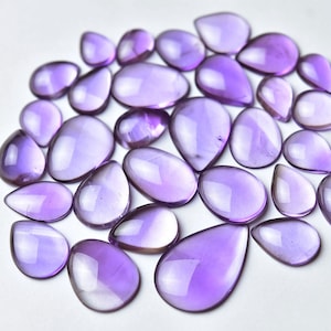 May include: A collection of 20 amethyst gemstone cabochons in various sizes and shades of purple. The cabochons are teardrop shaped and have a smooth, polished finish.