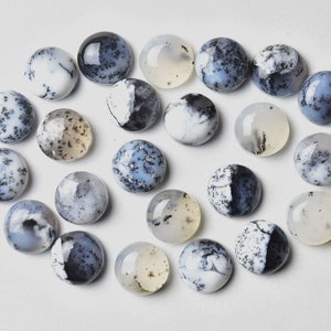 May include: A collection of 20 round, white, blue, and black dendritic opal cabochons. The cabochons are arranged in a loose circle on a white background.