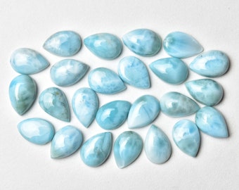 May include: A collection of 20 teardrop-shaped, light blue, iridescent gemstone cabochons. The cabochons are arranged in a semi-circle on a white background.