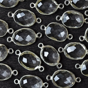 May include: A collection of clear quartz gemstone pendants with silver-toned jump rings. The pendants are oval-shaped and have a faceted finish.