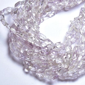May include: A strand of pale pink faceted amethyst beads. The beads are long and narrow, with a slightly irregular shape. The beads are strung on a clear thread.