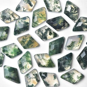 May include: A collection of faceted, diamond-shaped moss agate gemstones. The stones display a variety of green, white, and yellow patterns, with a polished, reflective surface. These gemstones are arranged on a white background.