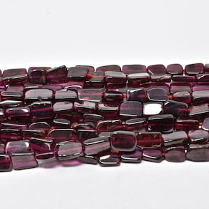 May include: Strand of rectangular, polished, dark red-purple gemstone beads. The beads are strung together on a red string, and are evenly sized. The beads have a glossy finish and are arranged against a white background.