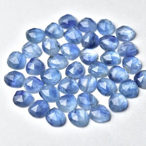Puede incluir: Un conjunto de gemas facetadas de color azul claro. Cada piedra tiene una forma triangular redondeada con m&uacute;ltiples facetas que capturan la luz. Las gemas est&aacute;n dispersas sobre una superficie blanca, creando un efecto brillante. Ideal para la creaci&oacute;n de joyas.