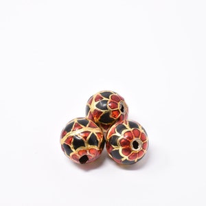 May include: Three round black beads with red and gold floral patterns. The beads are made of a smooth, shiny material.