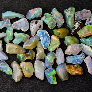 May include: A collection of small, iridescent opal stones in various shades of blue, green, and brown. The stones are irregularly shaped and have a natural, rough texture.