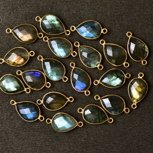 May include: A collection of 18 teardrop-shaped labradorite gemstone pendants with gold-toned jump rings. The stones are a mix of blue, green, and gold.
