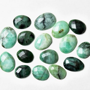 May include: A collection of 15 faceted emerald green gemstones, each with a unique shape and size. The stones are arranged in a loose cluster on a white background.
