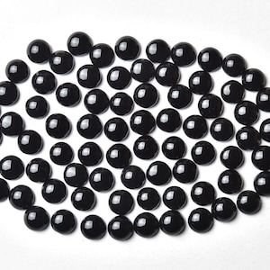 May include: A collection of black round glass beads, arranged in a circular pattern on a white background.