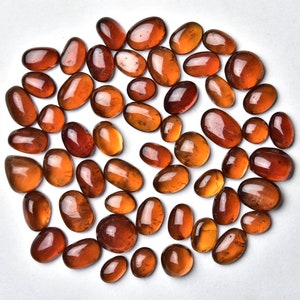 May include: A collection of approximately 40 smooth, oval-shaped, translucent, amber-colored gemstones. The stones are arranged in a circle on a white background.