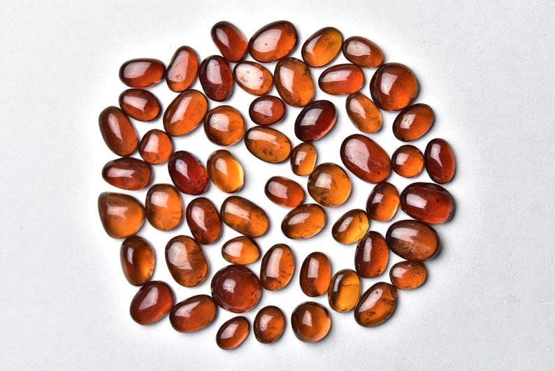 May include: A collection of approximately 40 smooth, oval-shaped, translucent, amber-colored gemstones. The stones are arranged in a circle on a white background.