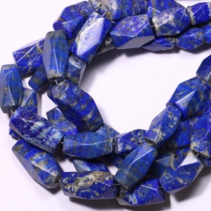 May include: A strand of dark blue lapis lazuli gemstone beads with a faceted, irregular shape. The beads are strung on a silver wire.
