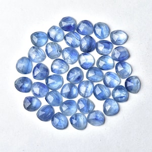 Puede incluir: Colecci&oacute;n de gemas facetadas de color azul claro. Cada piedra tiene una forma redondeada con m&uacute;ltiples facetas, creando un efecto brillante. Las gemas est&aacute;n dispersas sobre una superficie blanca, mostrando su color y claridad.