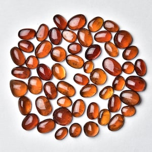 May include: A collection of approximately 40 brown and orange gemstone cabochons. The cabochons are oval shaped and have a smooth, polished finish.