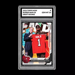 May include: A graded trading card featuring Rueben Bain Jr. in a red Buccaneers jersey with the number 1. The card is from the 2026 Topps Now Draft Rookie series and is graded GEM MT 10. The card shows Bain Jr. holding the jersey with another person.
