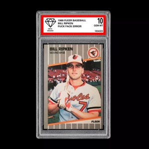 Peut inclure: Une carte de baseball classée mettant en vedette le deuxième but des Orioles de Baltimore, Bill Ripken. La carte est de la série 1989 Fleer Baseball et est classée GEM-MT 10 par Beckett Grading Services. La carte montre Ripken dans son uniforme des Orioles tenant une batte. La carte a une bordure blanche avec un fond gris.