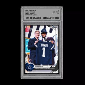 May include: A graded Caleb Downs Topps Now draft rookie card. The card features Downs holding a Dallas Cowboys jersey with the number 1. The card is graded GM 10 and has a serial number of 1010123. The card is encased in a protective holder.