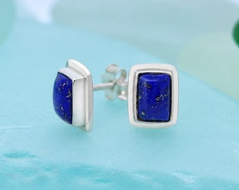 May include: A pair of stud earrings featuring rectangular lapis lazuli stones set in silver frames. Each earring has a deep blue stone with subtle gold-colored flecks, secured by a silver post and backing mechanism for pierced ears.
