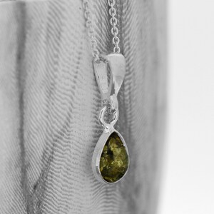 May include: A silver chain necklace with a teardrop-shaped pendant featuring a green amber stone.